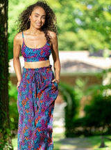 Model with hands in her pockets wearing a floral pattern organic cotton beach pants with elastic waistband with drawstring and tassel detail with matching bikini top
