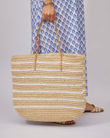 Person holding a striped straw bag with a blue patterned dress in the background