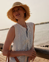 Woman wearing a straw hat and white lace top by a body of water.