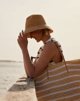 Woman on a beach holding a striped bag and wearing a hat