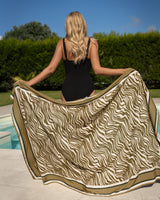 Woman holding a patterned towel by a poolside with greenery in the background