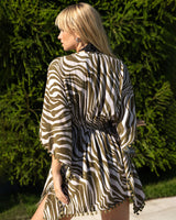 Woman wearing a zebra print dress standing against a green hedge.