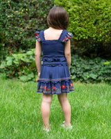 Child wearing a blue dress with floral embroidery in a garden setting