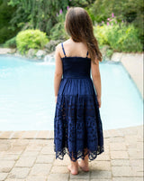 Girl in a navy lace dress standing by a pool with greenery in the background