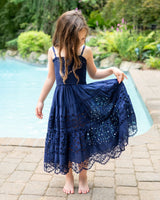 Young girl in a navy blue lace dress standing by a pool with greenery in the background
