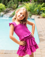 Young girl in a pink dress standing by a pool with a garden in the background