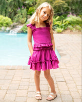 Young girl in a pink dress standing by a pool with greenery in the background