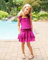 Young girl in a pink dress standing by a pool with greenery in the background