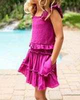 Child wearing a pink dress by a poolside with blurred greenery in the background