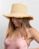Woman wearing a straw hat and pink top against a plain background