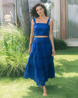 Woman in a blue dress standing on grass with plants and a building in the background