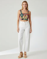 Woman wearing a floral crop top and white pants on a white background