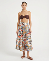 Woman wearing a strapless brown bikini top and a colorful floral skirt on a white background