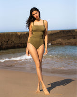 Woman in a green swimsuit standing on a beach with clear blue sky.