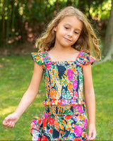Young girl in a colorful dress standing in a grassy area with trees in the background
