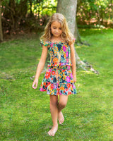 Young girl in a colorful dress standing on grass with trees in the background
