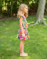 Young girl in a colorful dress standing on grass with trees in the background