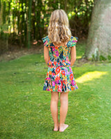Young girl in a colorful dress standing on grass with trees in the background