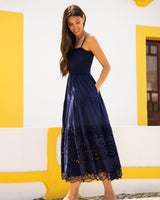 Woman wearing a navy blue dress with lace details against a yellow and white wall.