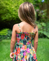 Child wearing a colorful floral dress standing outdoors with greenery in the background
