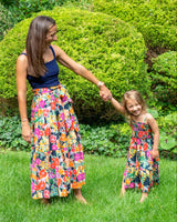 Woman and child holding hands in a garden with manicured hedges and flowers.