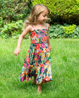Young girl in a colorful dress running on grass with greenery in the background