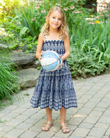 Young girl in a blue patterned dress holding a blue and white ball in a garden setting.