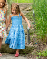 Two young girls, one in a blue dress and the other in a floral dress, standing on rocks in a natural setting.