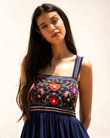 Woman wearing a navy blue dress with colorful floral embroidery against a plain background