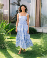 Woman in a blue floral dress standing on grass with a building in the background