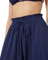 Close up shot of model wearing navy blue organic cotton beach pants with elastic waistband with drawstring and tassel detail