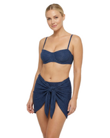 A woman modeling a two-piece swimwear set consisting of a textured navy blue bralette and a matching navy blue wrap skirt with a front knot detail, set against a plain white studio background.