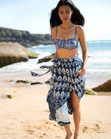 Woman in a blue and white patterned bikini and sarong on a beach.