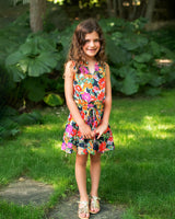 Young girl in a colorful dress standing on grass with greenery in the background