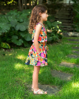 Young girl in a colorful dress standing on grass with a garden background