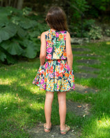 Young girl in a colorful dress standing on a grassy path with a garden background