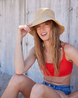 Woman wearing a red bikini top and straw hat against a concrete wall.