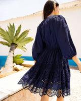 Woman in a navy blue lace dress standing by a beach with palm trees.