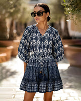 Woman wearing a blue patterned dress with sunglasses outdoors.