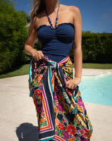 Woman wearing a blue strapless top and colorful floral skirt by a pool.