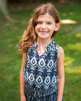 Young girl wearing a blue patterned dress standing outdoors with green grass in the background