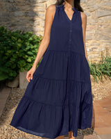 Woman wearing a navy blue tiered dress standing outdoors against a stone wall.