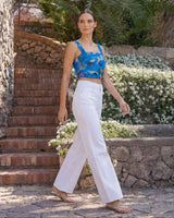 Woman in a blue top and white pants standing in a garden with stone walls and plants.