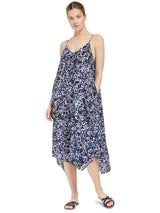 Model posing with hands in her pocket wearing a black and white leopard print strappy and long flowy dress with adjustable back shoulder straps, and v-neckline front and back with black sandals