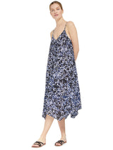 Model posing with hands behind her back wearing a black and white leopard print strappy and long flowy dress with adjustable back shoulder straps, and v-neckline front and back with pockets and black sandals