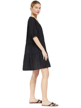 the side of a model wearing a black slightly above the knee dress with rounded neckline and short puff sleeve with a covered elastic cuff
