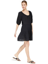 model wearing a black slightly above the knee dress with rounded neckline and short puff sleeve with a covered elastic cuff with black sandals