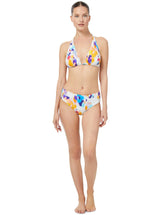 Brunette model posses wearing bikini halter top and mid rise bikini bottoms in floral ikat print with white background.