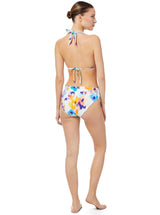Brunette model posses away tilting head over shoulder. She is wearing bikini halter top and mid rise bikini bottoms in floral ikat print with white background.