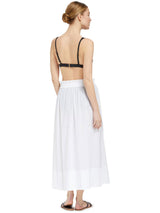 the back of a model model wearing fresh white midi length skirt with side slits and elastic waistband with drawstring detail with black  bikini top with gold clasp and black sandals